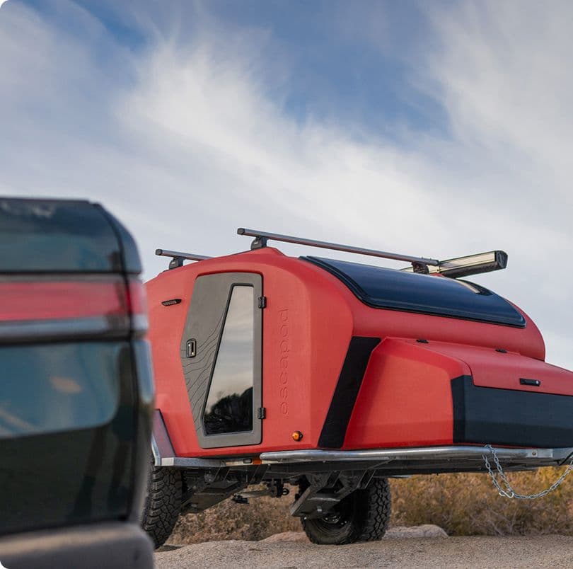 A green TOPO2 fiberglass camping trailer is parked on a rocky outcropping with a backdrop of a red rock mesa in the distance.
