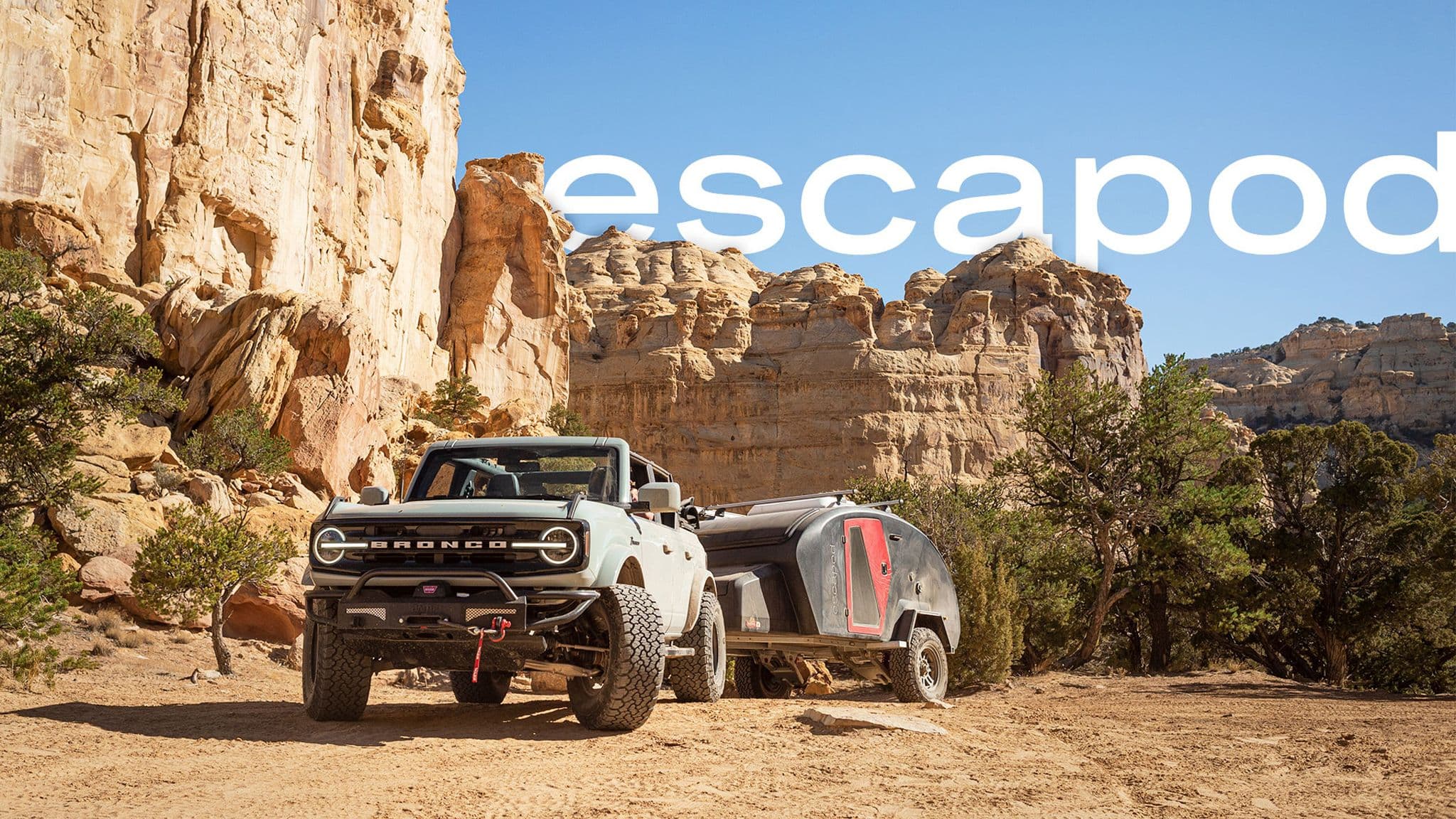 Escapod trailer towed by a Ford Bronco through a rugged desert landscape with towering rock formations.