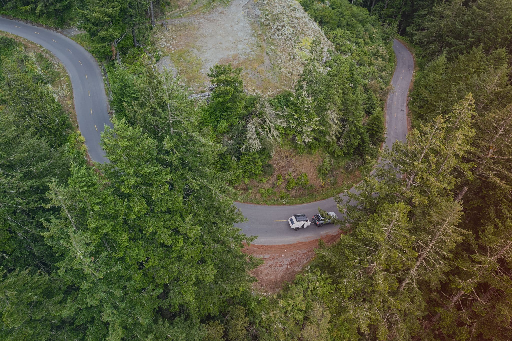 A winding forest road seen from above, with an Escapod TOPO2 trailer being towed through lush greenery, showcasing its off-road capability.