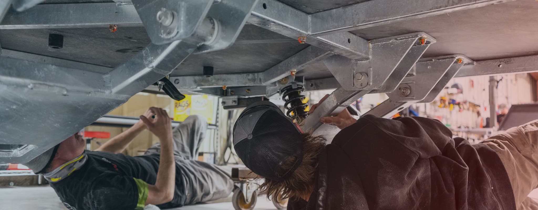 Two craftsmen at Escapod Trailers working on the Freeride Suspension underneath a TOPO2 off-road teardrop trailer.