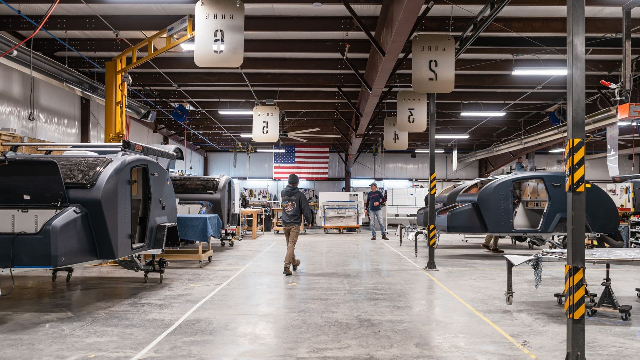 A wide view of the Escapod factory floor, with multiple trailer bodies in various stages of production and employees working under numbered workstations.