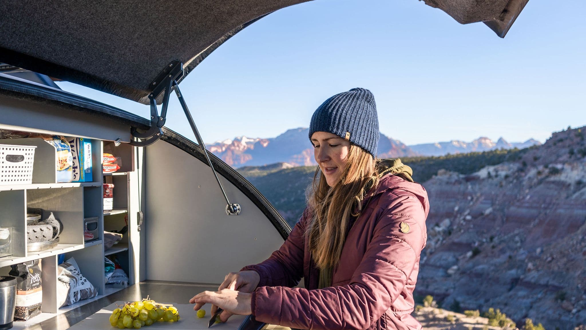 Woman preps food in the rear galley of an Escapod trailer, surrounded by breathtaking canyon views, highlighting the kitchen's spacious layout.