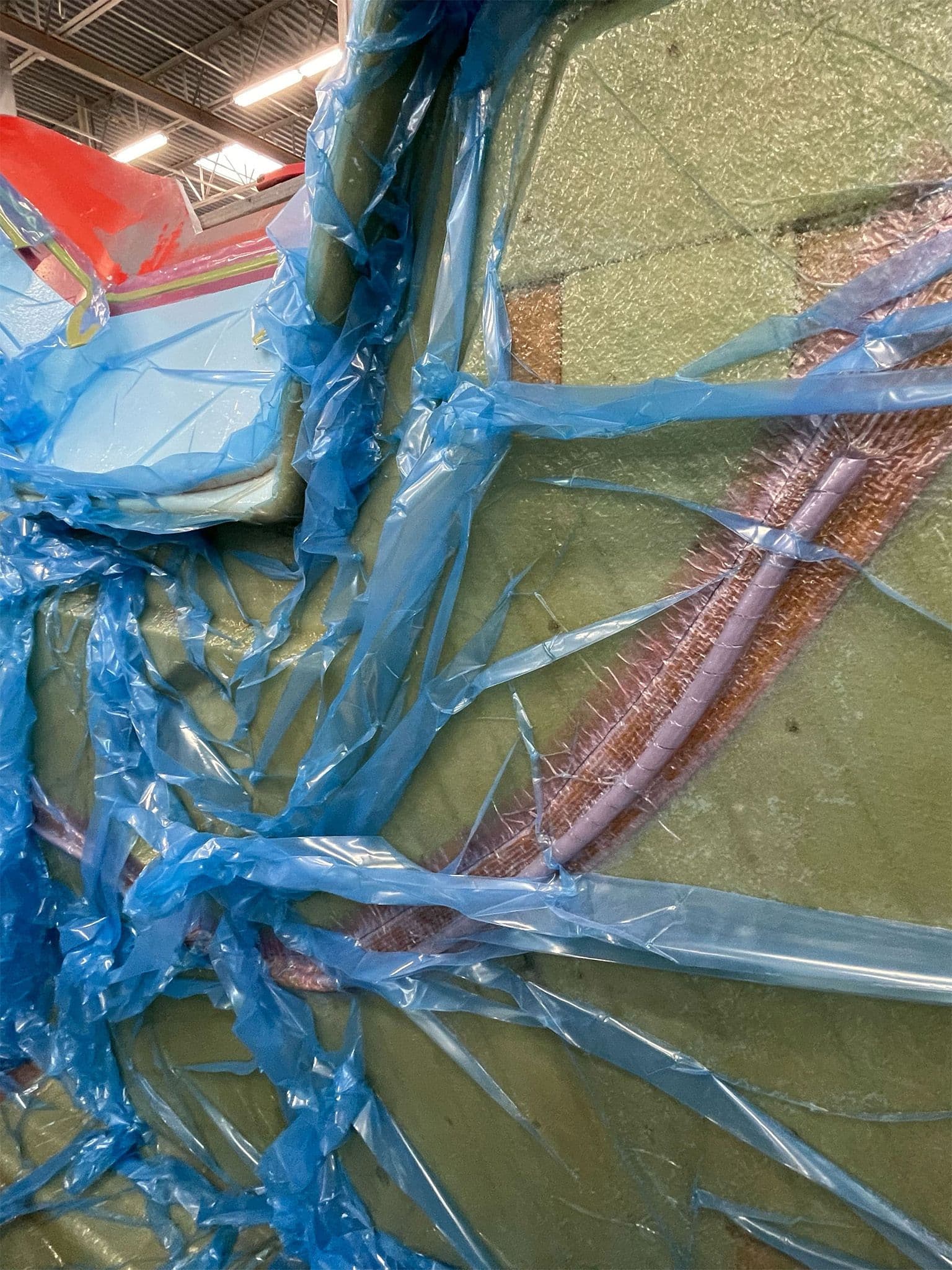 Detailed view of the fiberglass vacuum infusion process with blue vacuum bagging material and tubing covering a trailer mold.