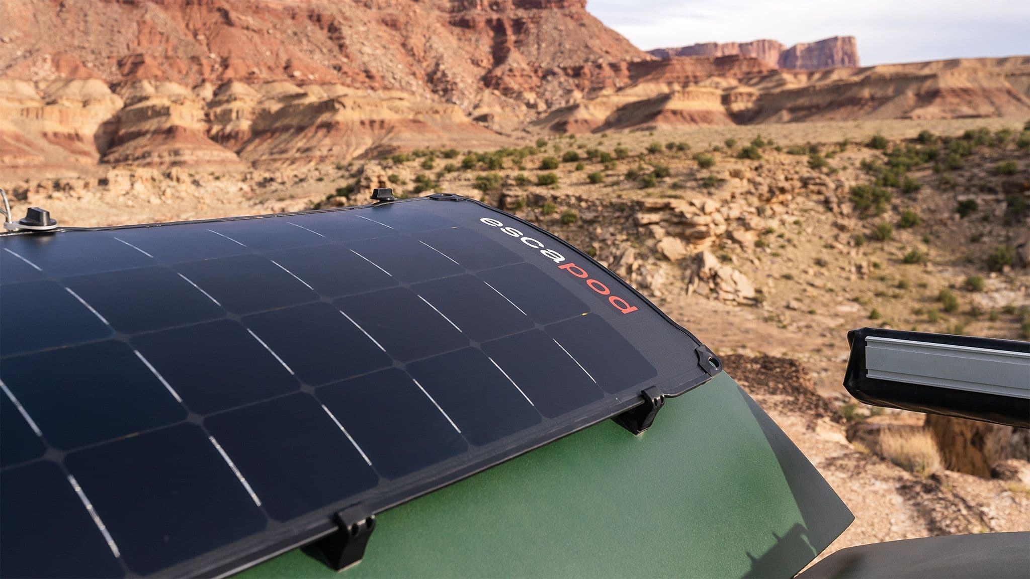 A 140W solar panel mounted on the back of a green Escapod TOPO2, with an awning visible on mounted to the side, and a desert landscape in the background.