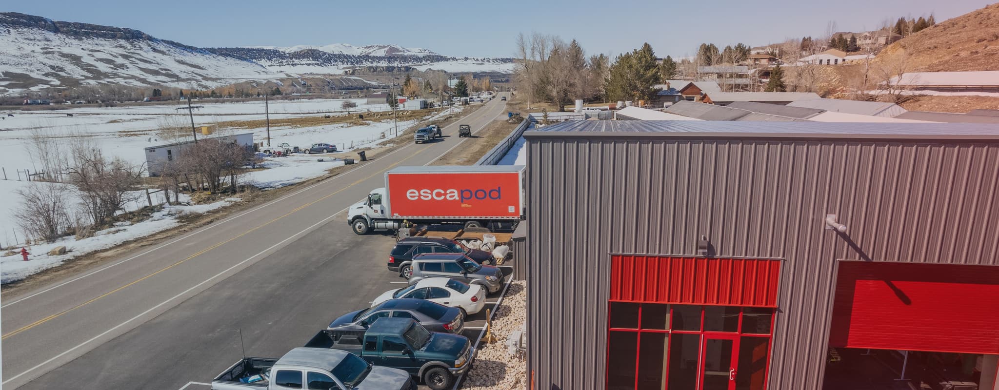 Escapod’s facility on a snowy day with a red Escapod-branded truck outside, set in a rural area with mountains visible in the distance.