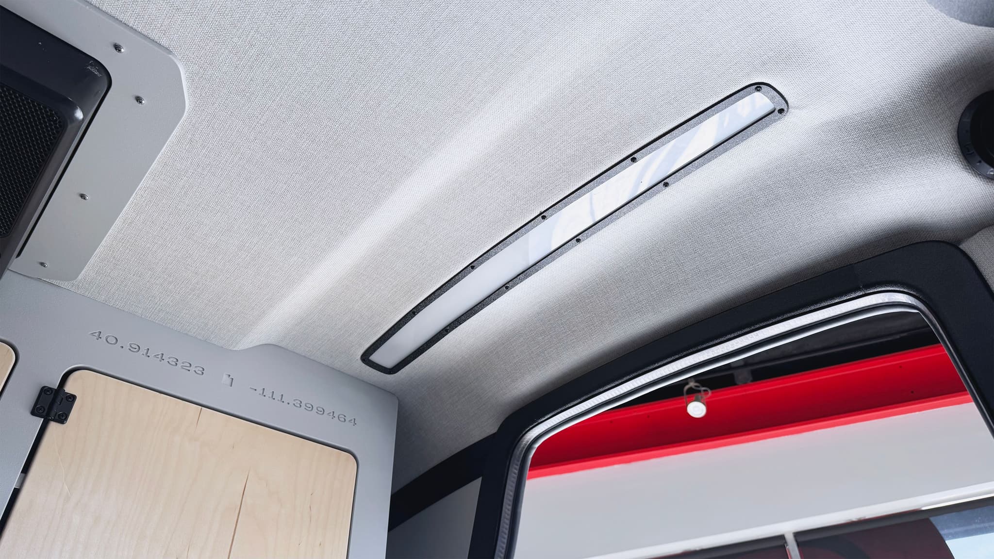 An interior view of the escapod topo2 trailer with the dimmable LED lights running alongside the interior headliner, with the cabinet and the entry door also in view.