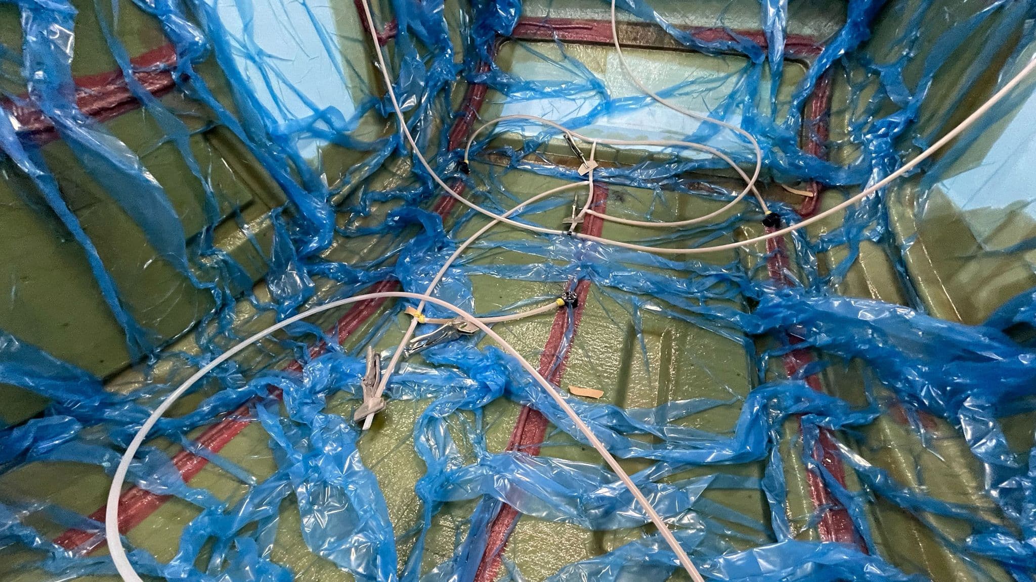 Close-up of the fiberglass layup inside the mold, showing infusion tubes and resin channels covered in blue sheeting.