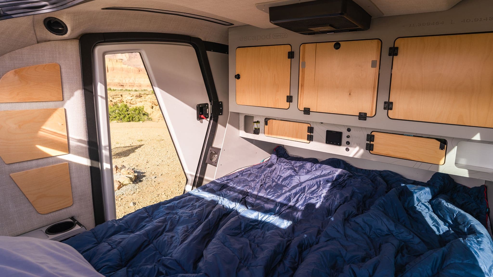 Inside view of the Escapod TOPO2, featuring a neatly made bed with storage cabinets and a soft glow from natural daylight.