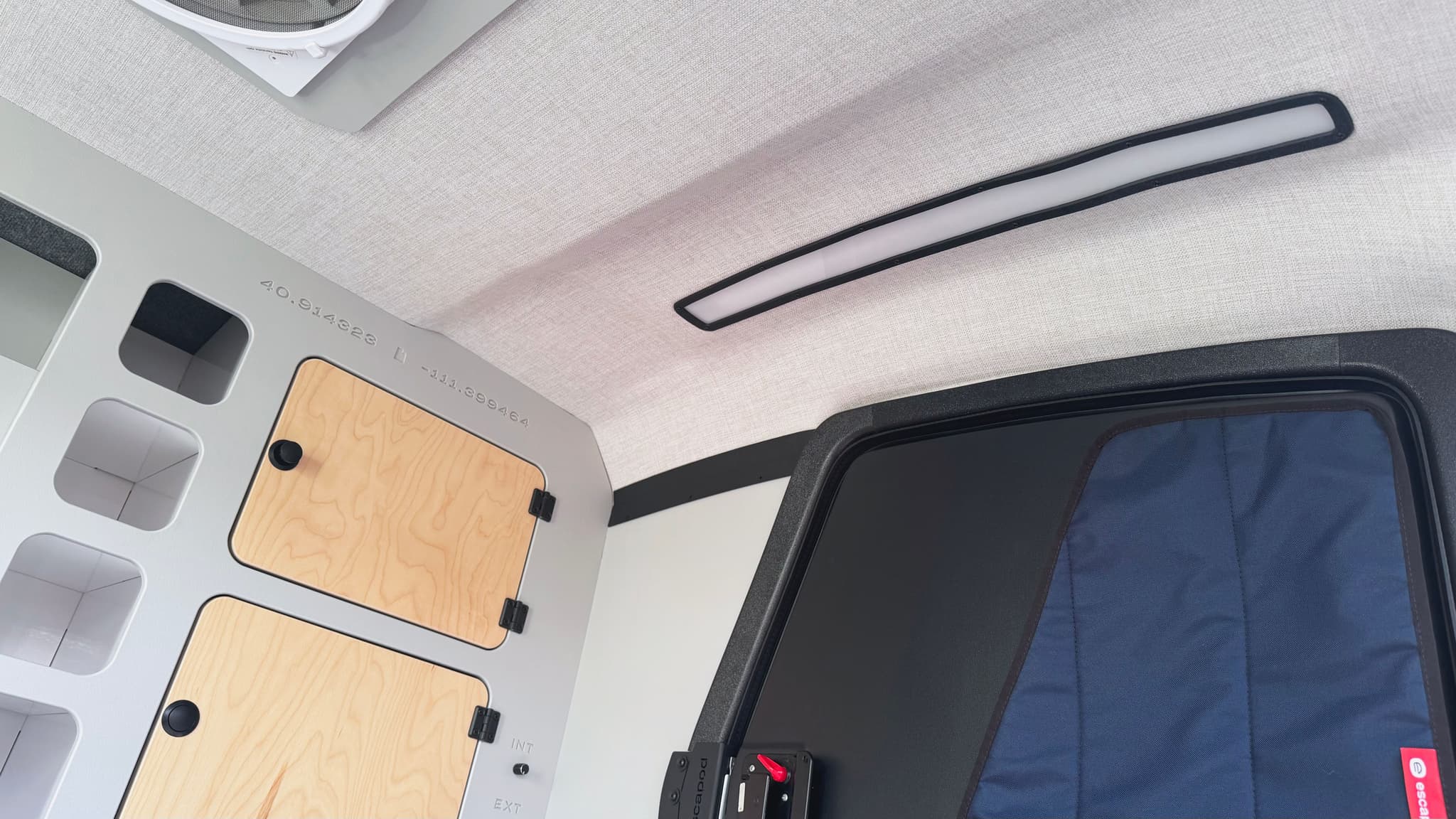 A detail shot of the interior of an Escapod TOPO2 Nomad, with LED light bar, cabinets, cubbies, and a black entry door with a blackout window cover.