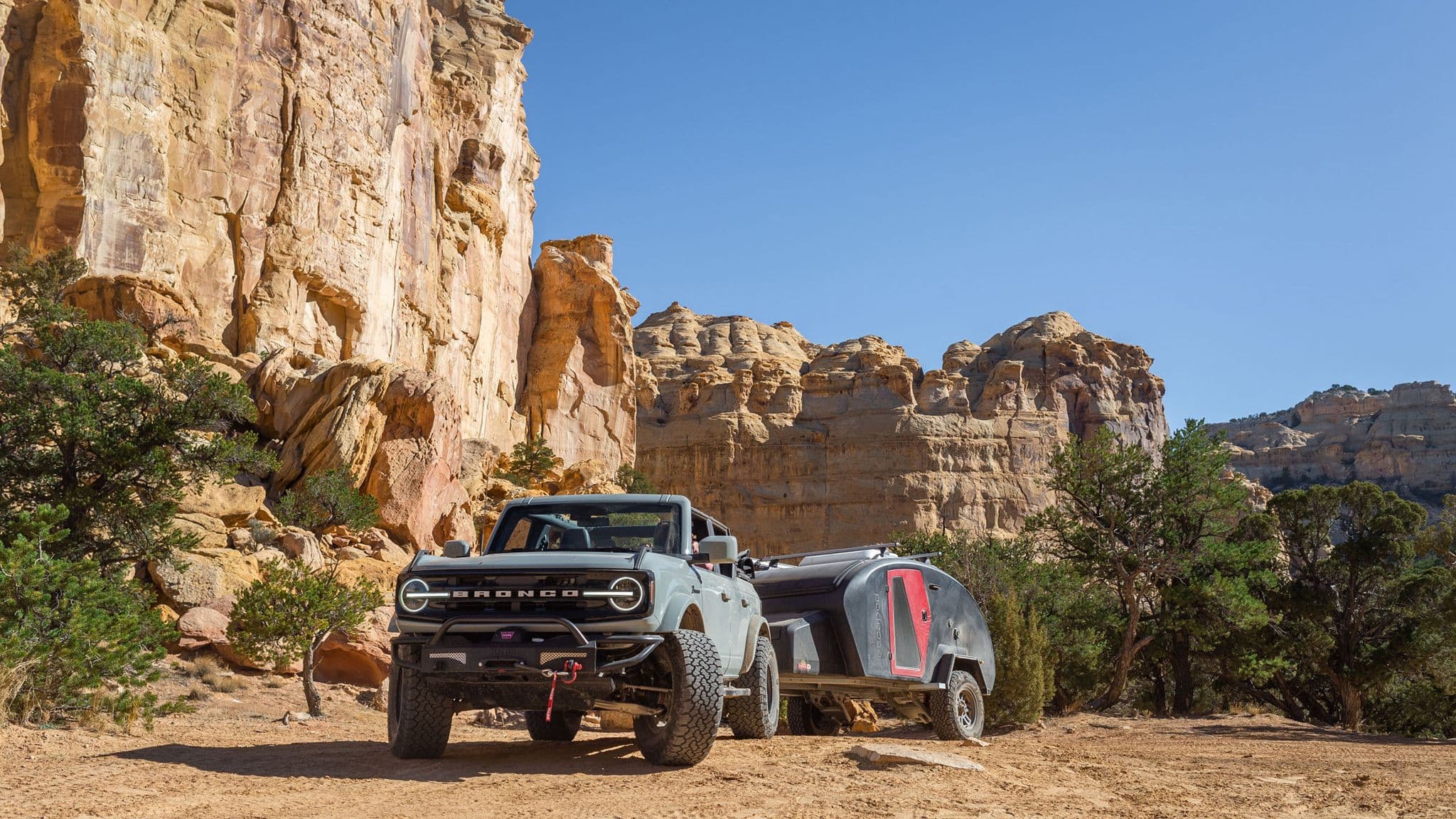 Escapod off-road camper trailer hitched to a Ford Bronco, parked against a breathtaking desert canyon backdrop under a clear blue sky.