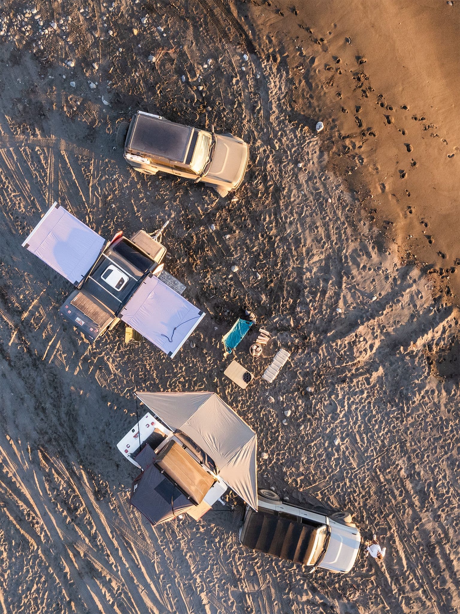 Two Escapod TOPO2s with awning extended set up at camp on the pacific ocean beach along with two Ford Broncos at golden hour.