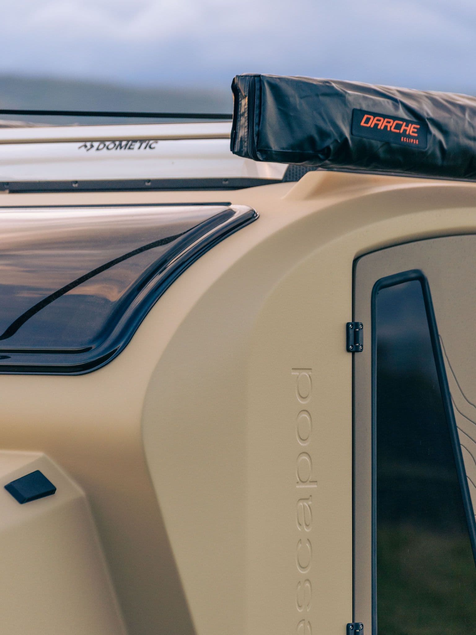 Close-up of an Escapod TOPO2 trailer’s side panel, showcasing its embossed branding and a roof-mounted Darche awning.