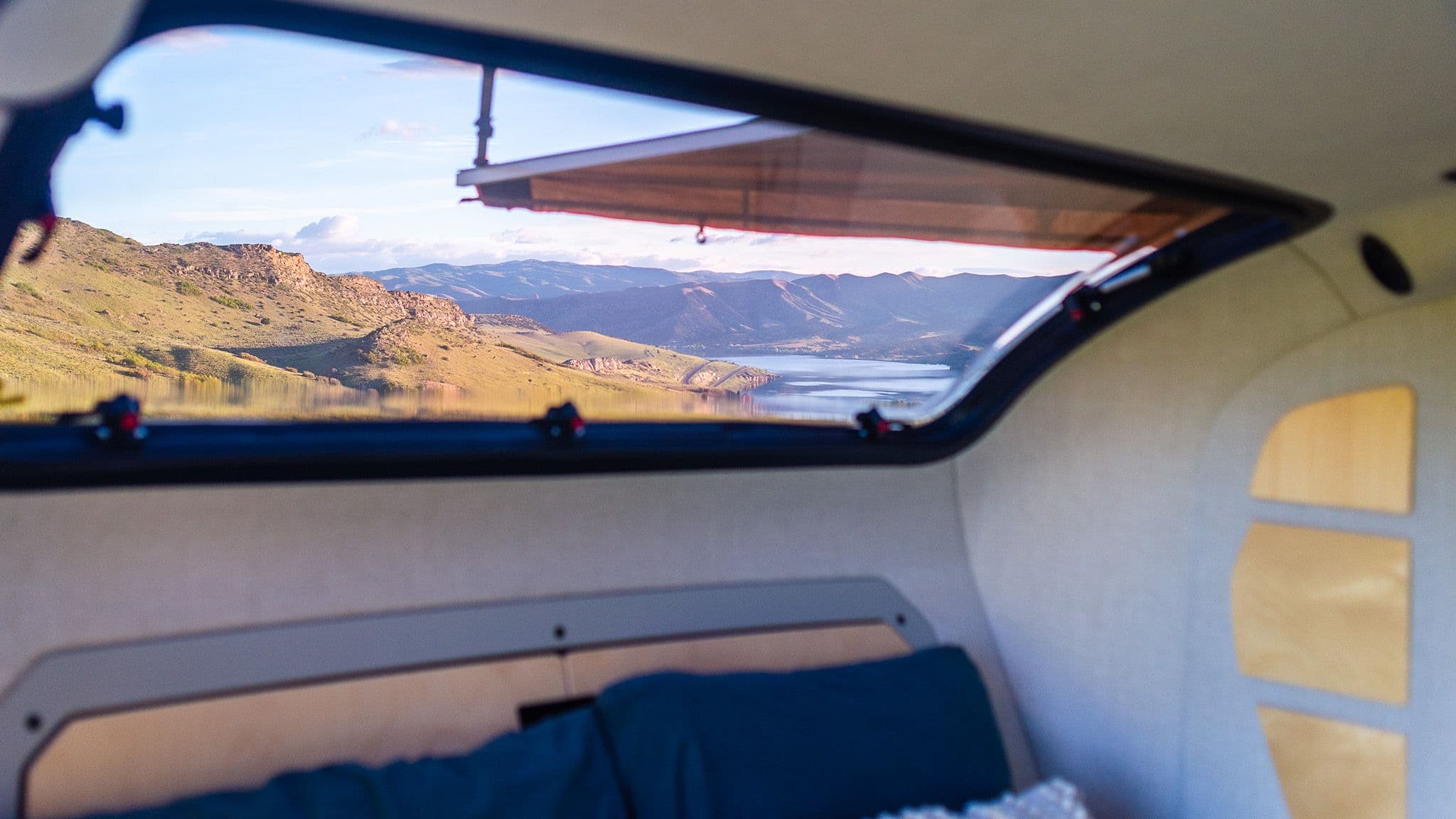 The large stargazer window of the TOPO2, showing vast mountain views at sunrise with a lake in the background.