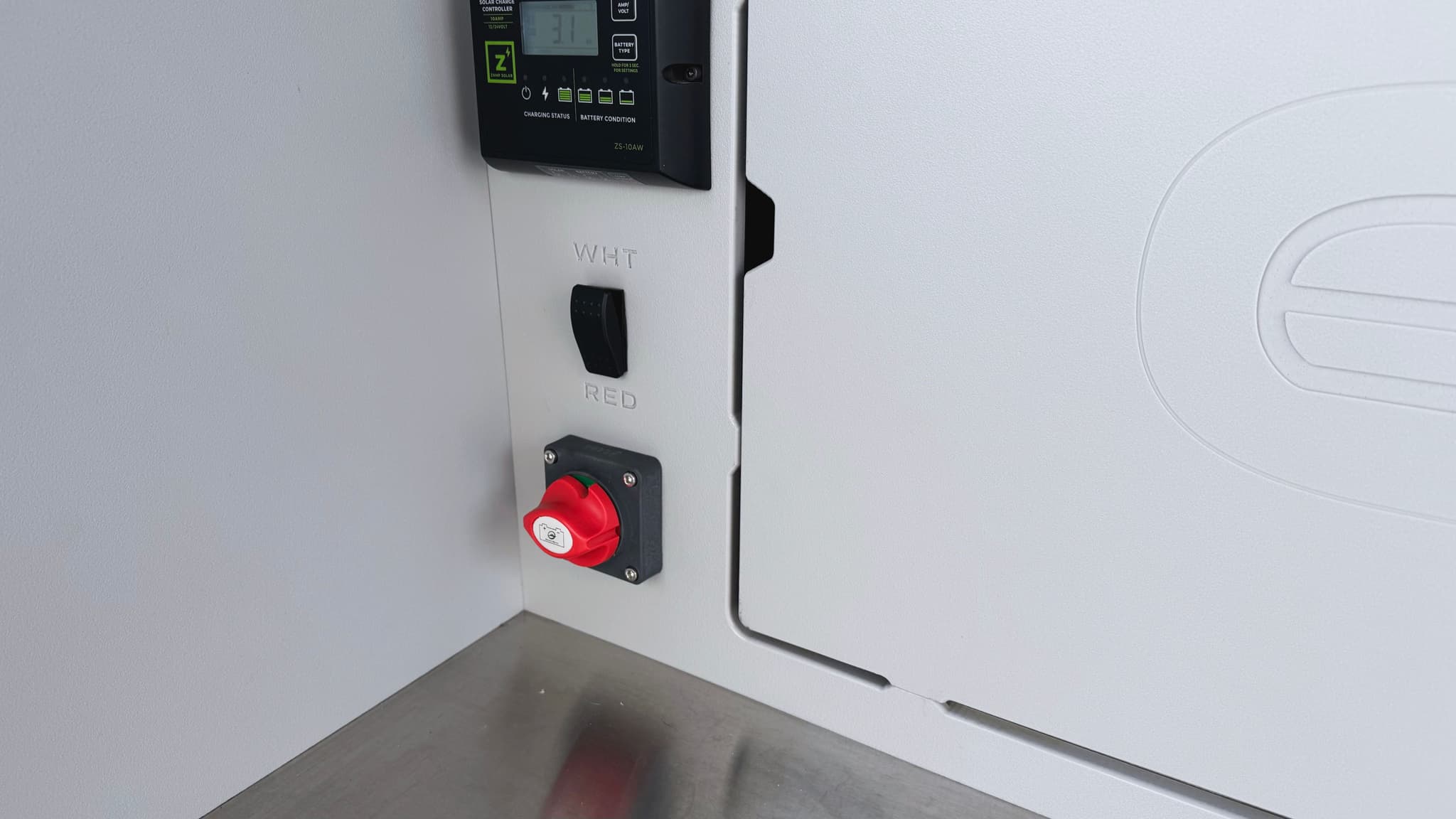 A detail view of the galley of an Escapod TOPO2 Nomad, showing the battery cutoff switch, the solar controller, and a light switch that toggles between white and red LED light.