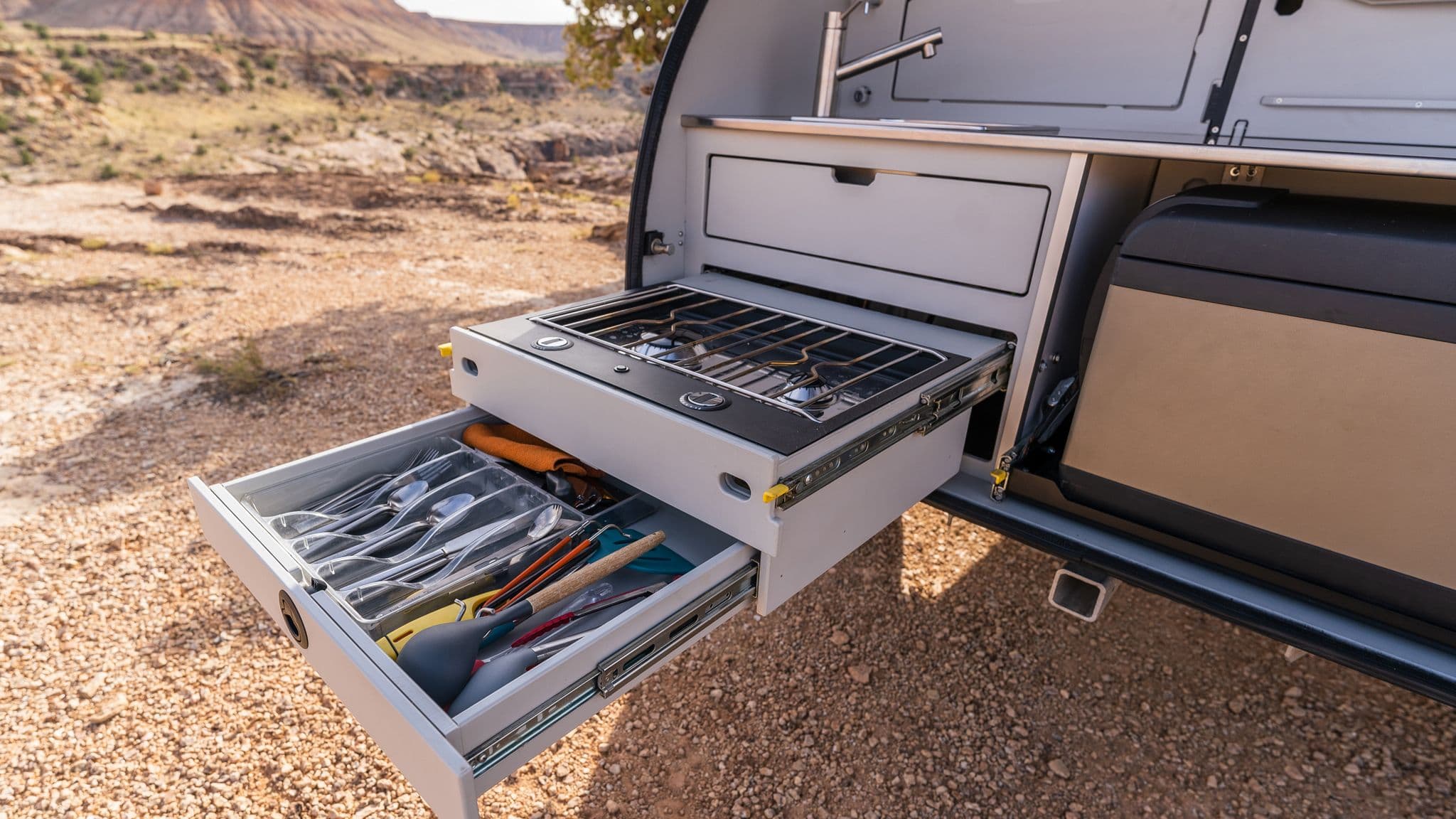 A well-organized TOPO2 galley kitchen with a slide-out two-burner stove, utensils drawer, and a compact refrigerator for off-grid cooking.