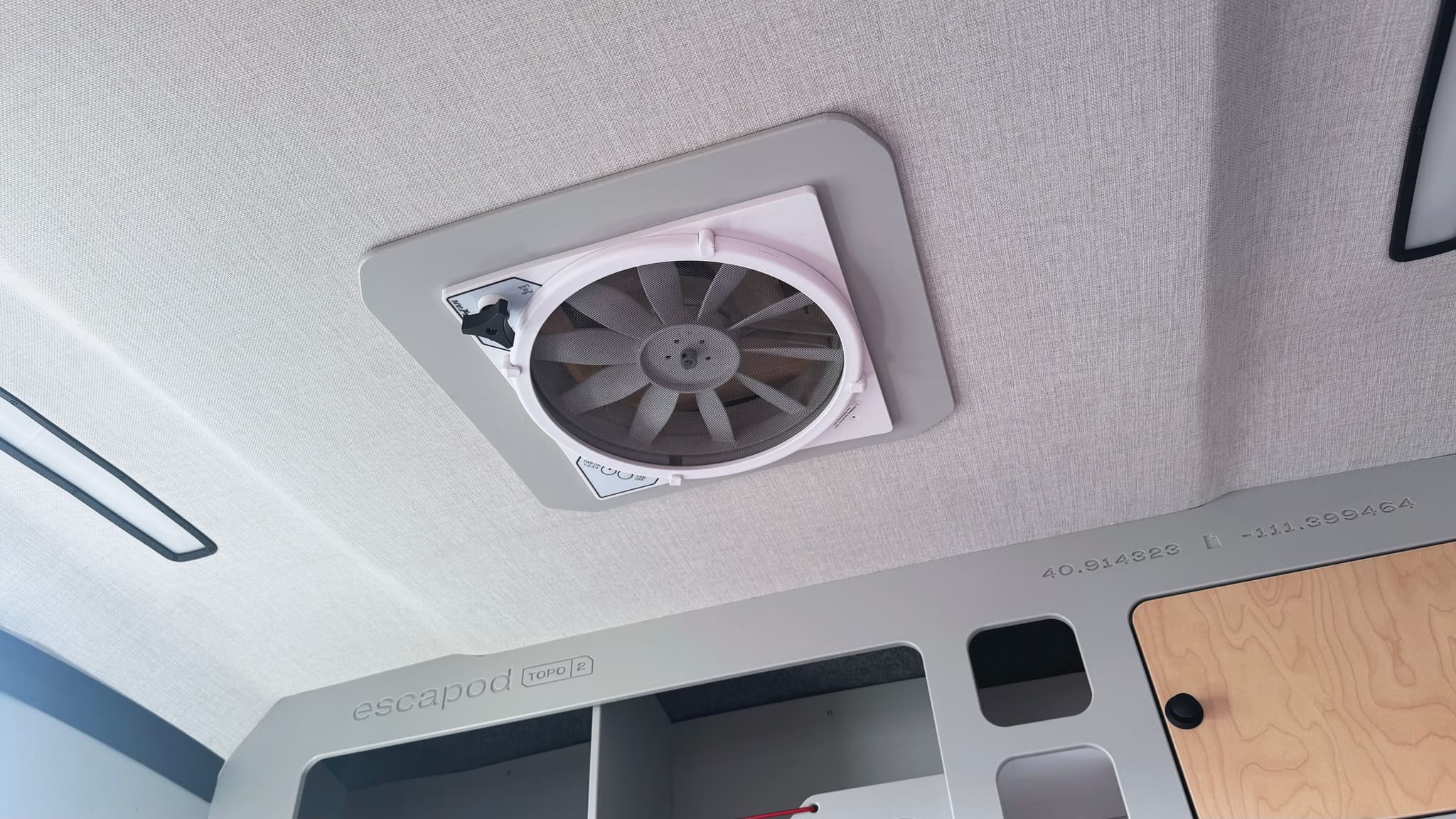 A wide angle view of the interior of an Escapod TOPO2 Nomad, showing the MaxxFan vent, and the cabinet structure behind the fan.