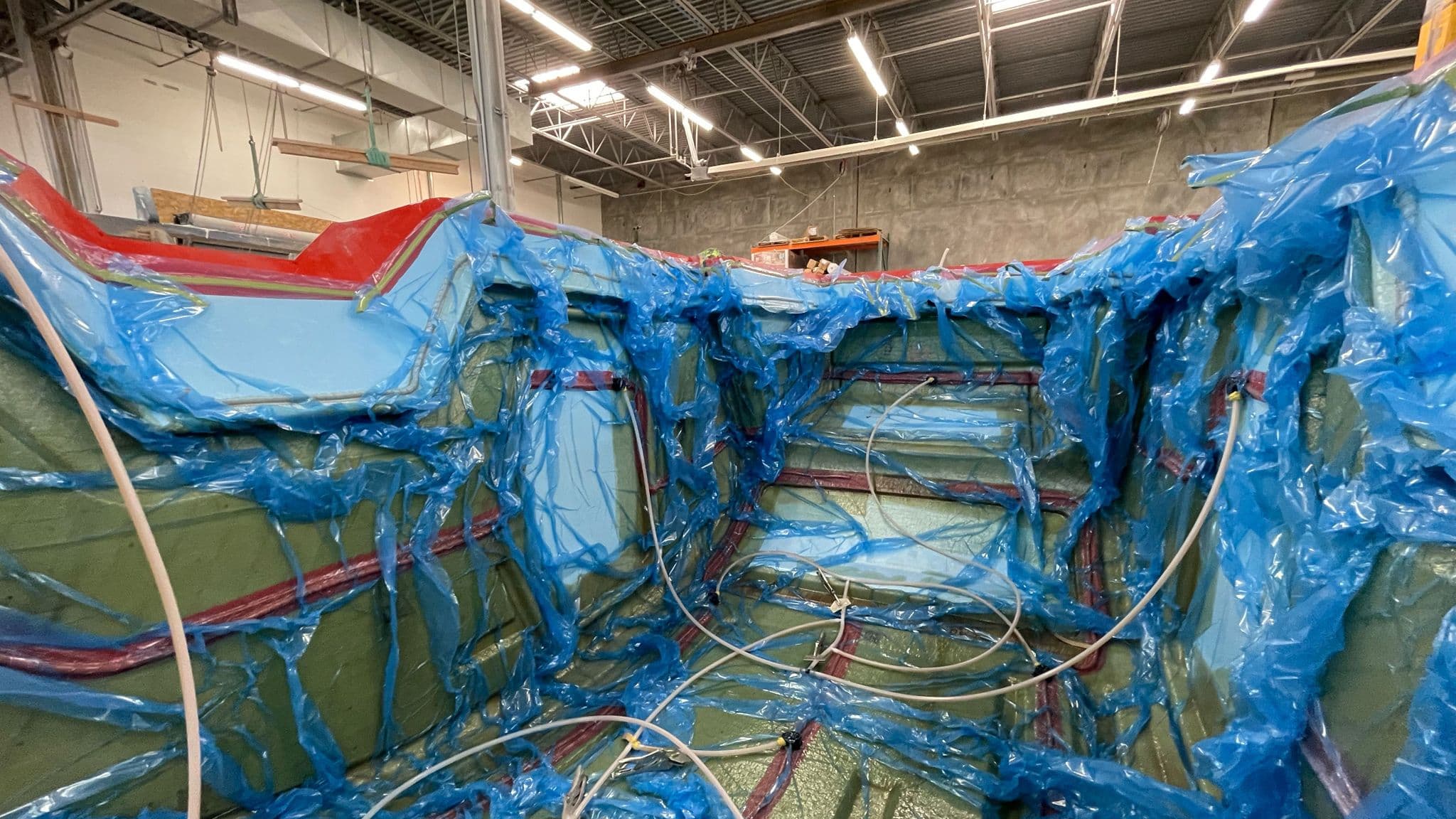 A fiberglass mold encased in blue vacuum bagging material with visible resin infusion lines inside a large production facility.