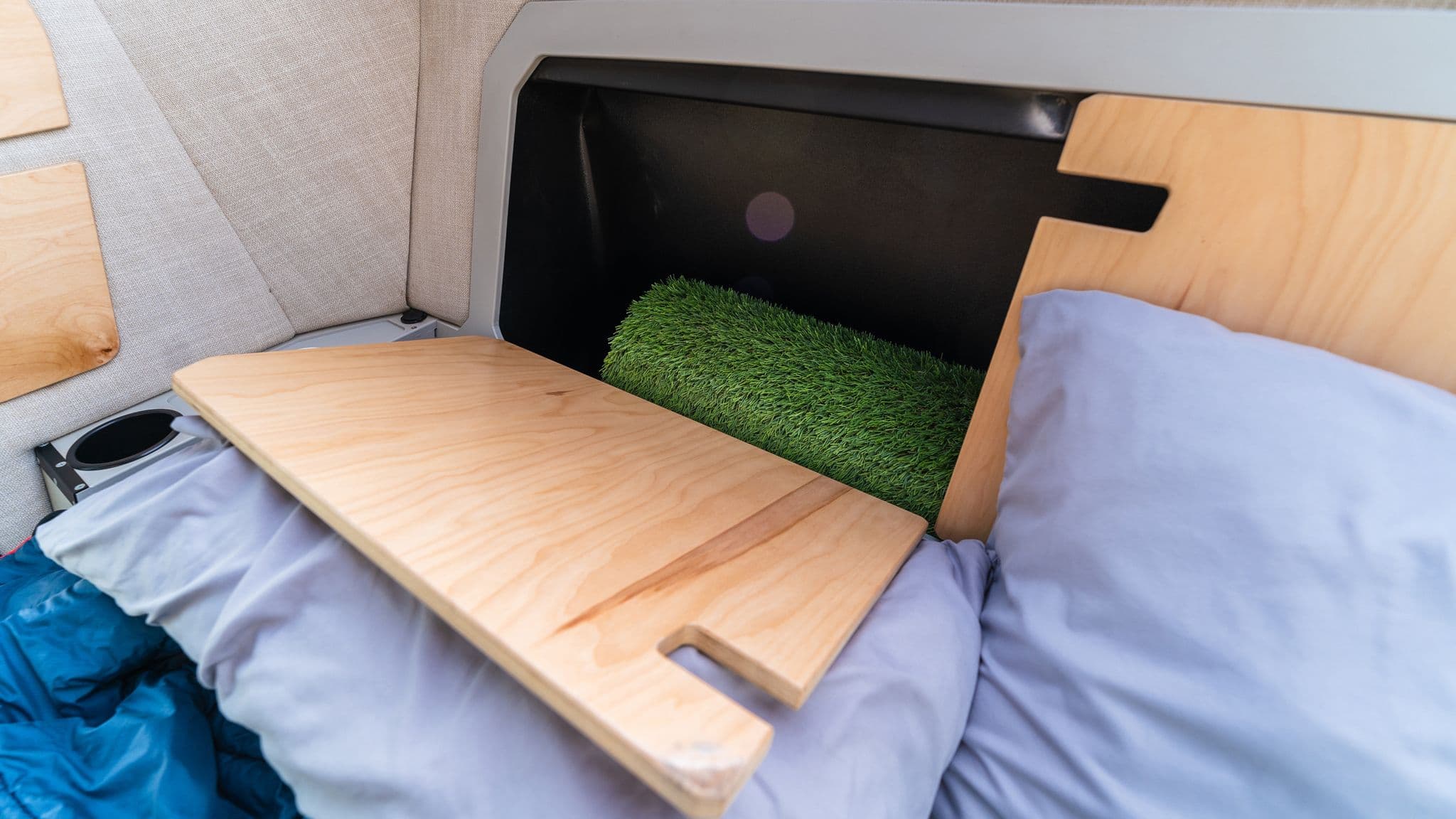 A close-up of an Escapod TOPO2 teardrop trailer's interior storage compartment with a wooden cover, revealing artificial grass mat storage.