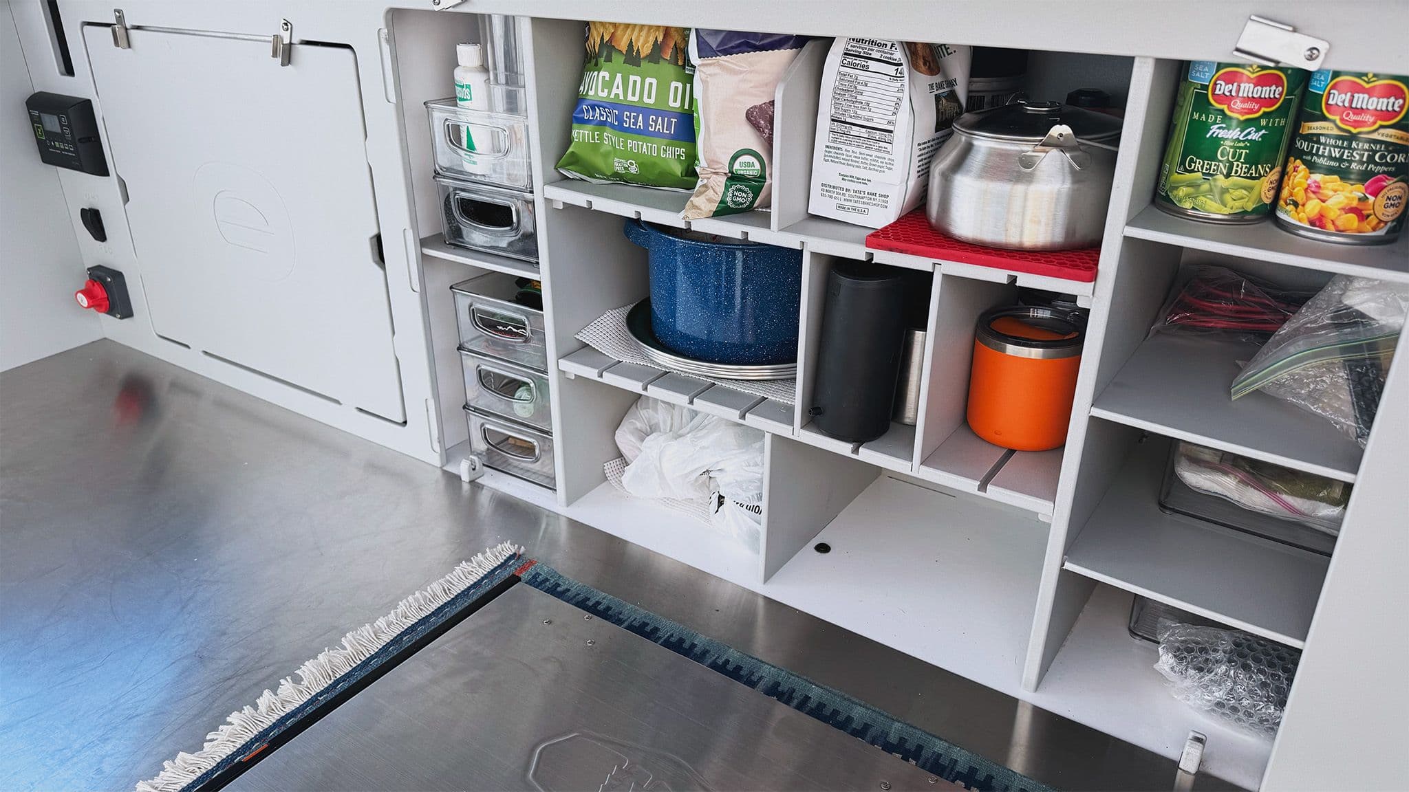 The back galley of an Escapod TOPO2 Nomad, showing the cabinet face removed to reveal adjustable cabinets full of kitchen goods for camping.