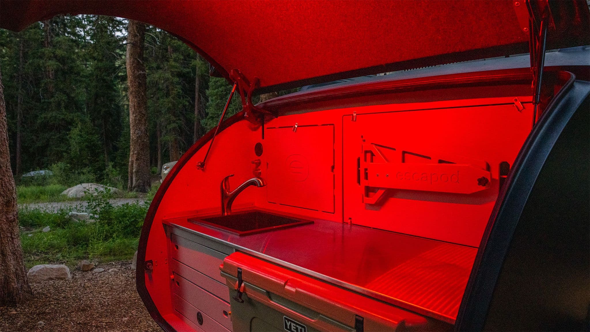The galley of an Escapod TOPO2, shown at night with red lighting casting color across the countertop and cabinets.